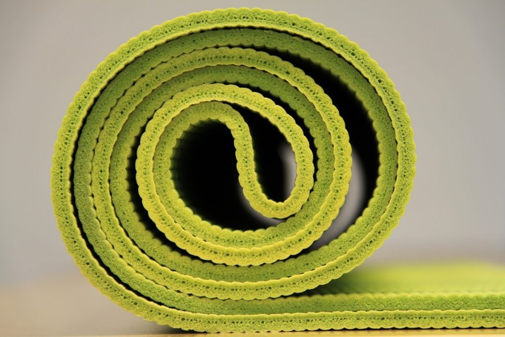 aufgerollte grüne Yoga-Matte vor weißem Hintergrund