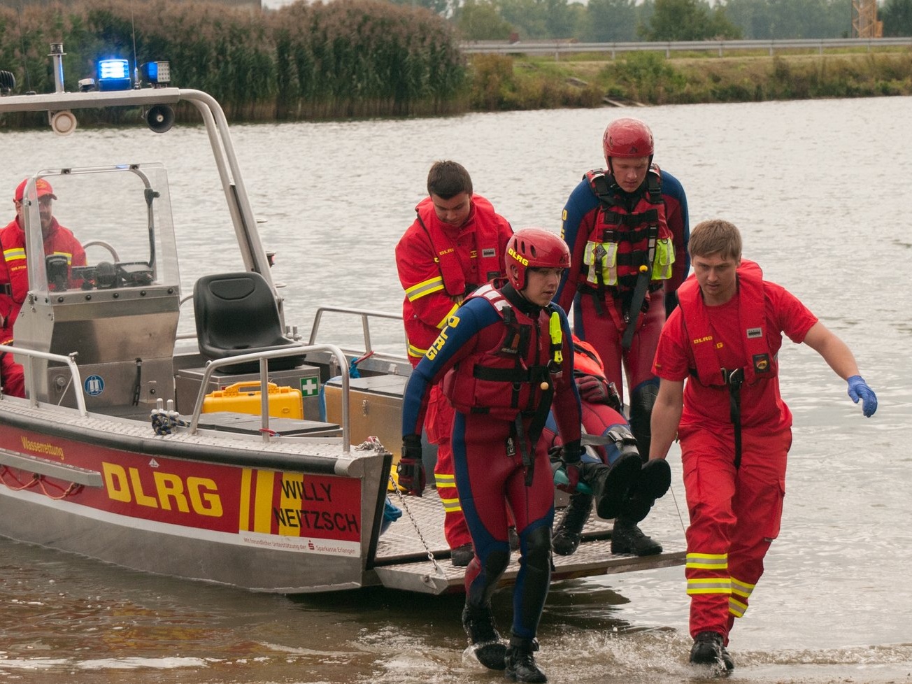 DLRG-Einsatzkräfte tragen eine Person vom Rettungsboot an Land